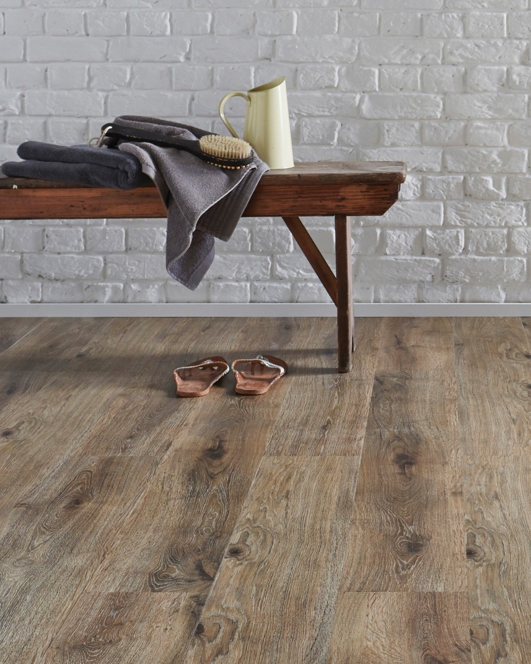 Rustic oak laminate plank flooring with a reclaimed bench against a white-brick wall